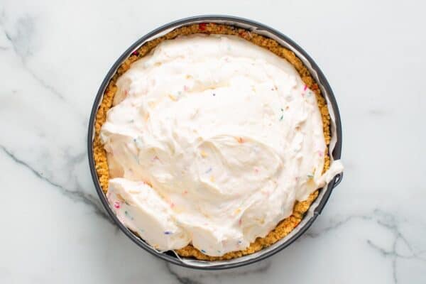 cheesecake batter with sprinkles added to a springform pan with a cookie crust.