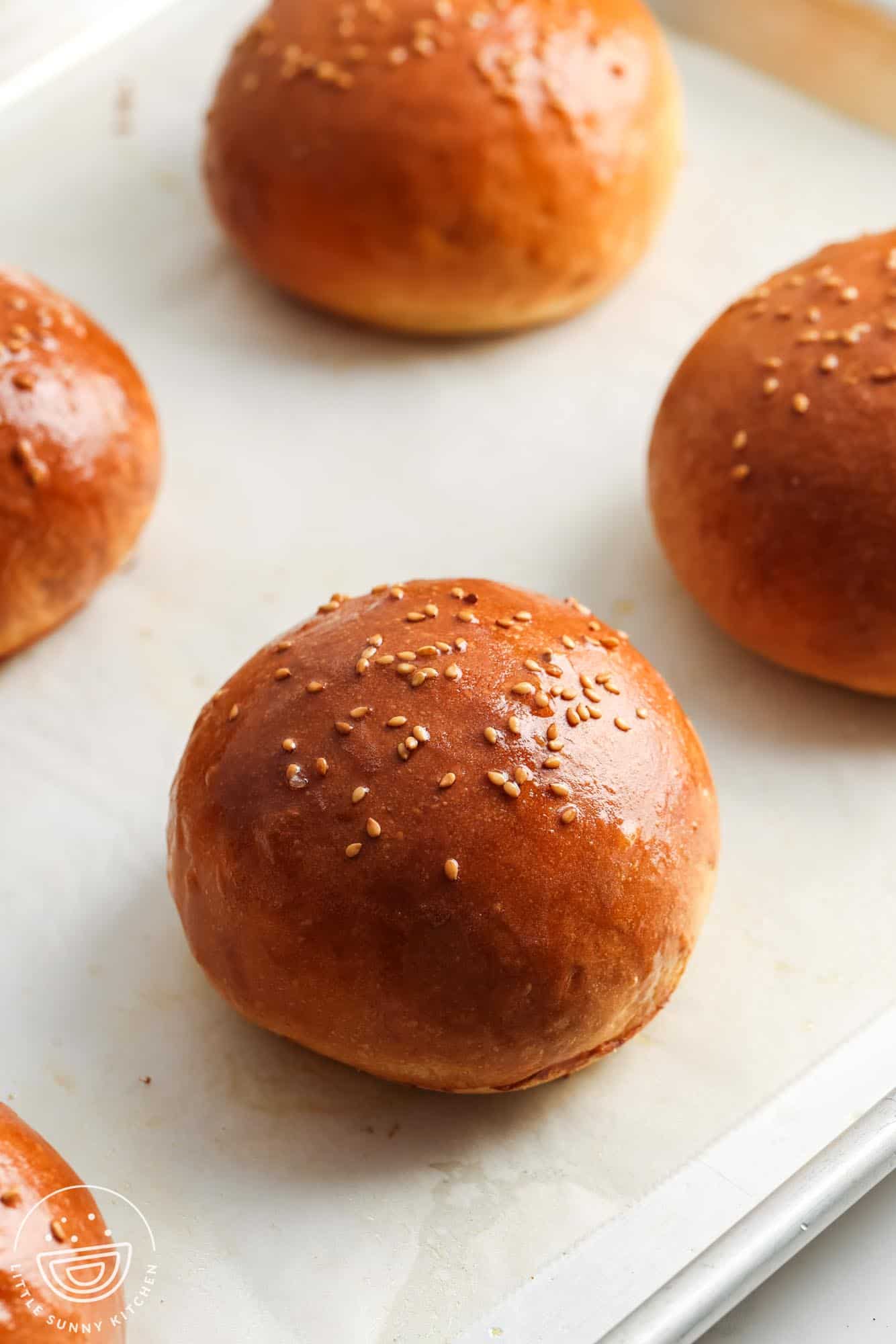 homemade hamburger buns topped with sesame seeds on a parchment lined baking sheet.