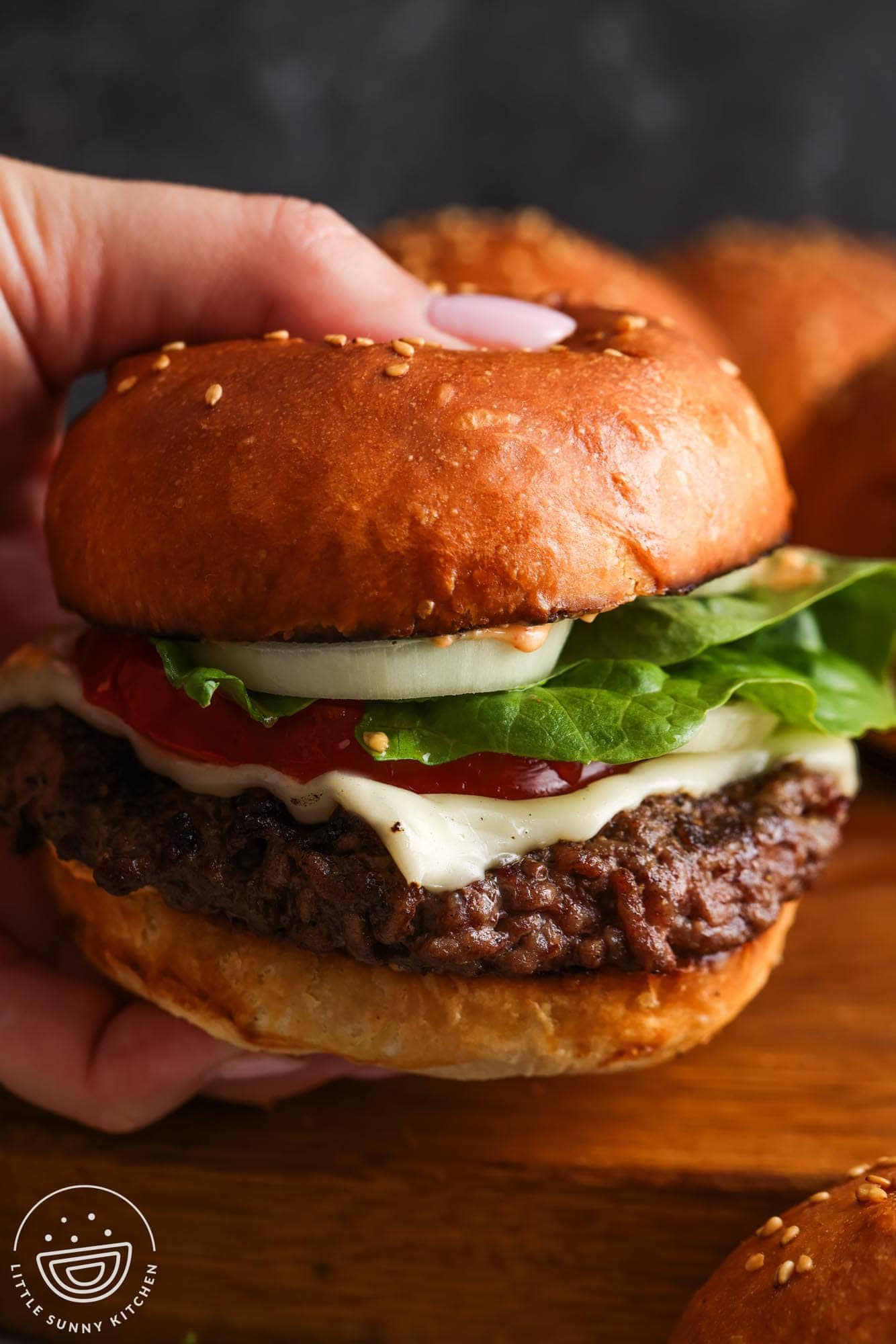 a hand holding a cheeseburger with toppings that is on a homemade toasted hamburger bun.
