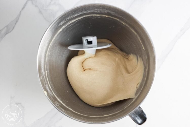 Dough for hamburger buns on a metal mixer bowl with the dough hook attachment.