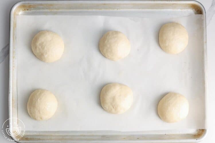 unbaked hamburger buns on a metal pan lined with parchment paper.