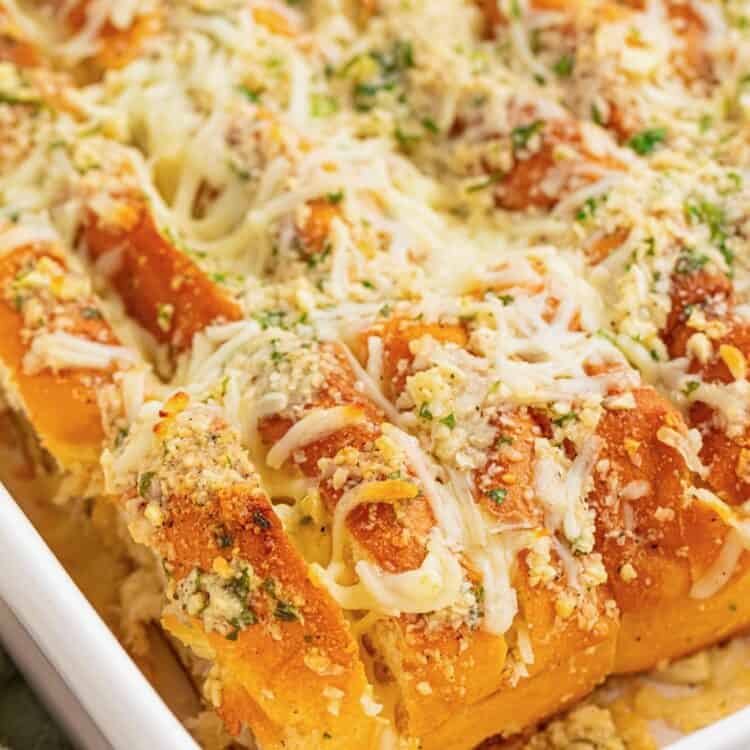 sliced hawaiian roll garlic bread in a white ceramic baking dish. The buns are covered in cheesy garlic butter and chopped herbs.