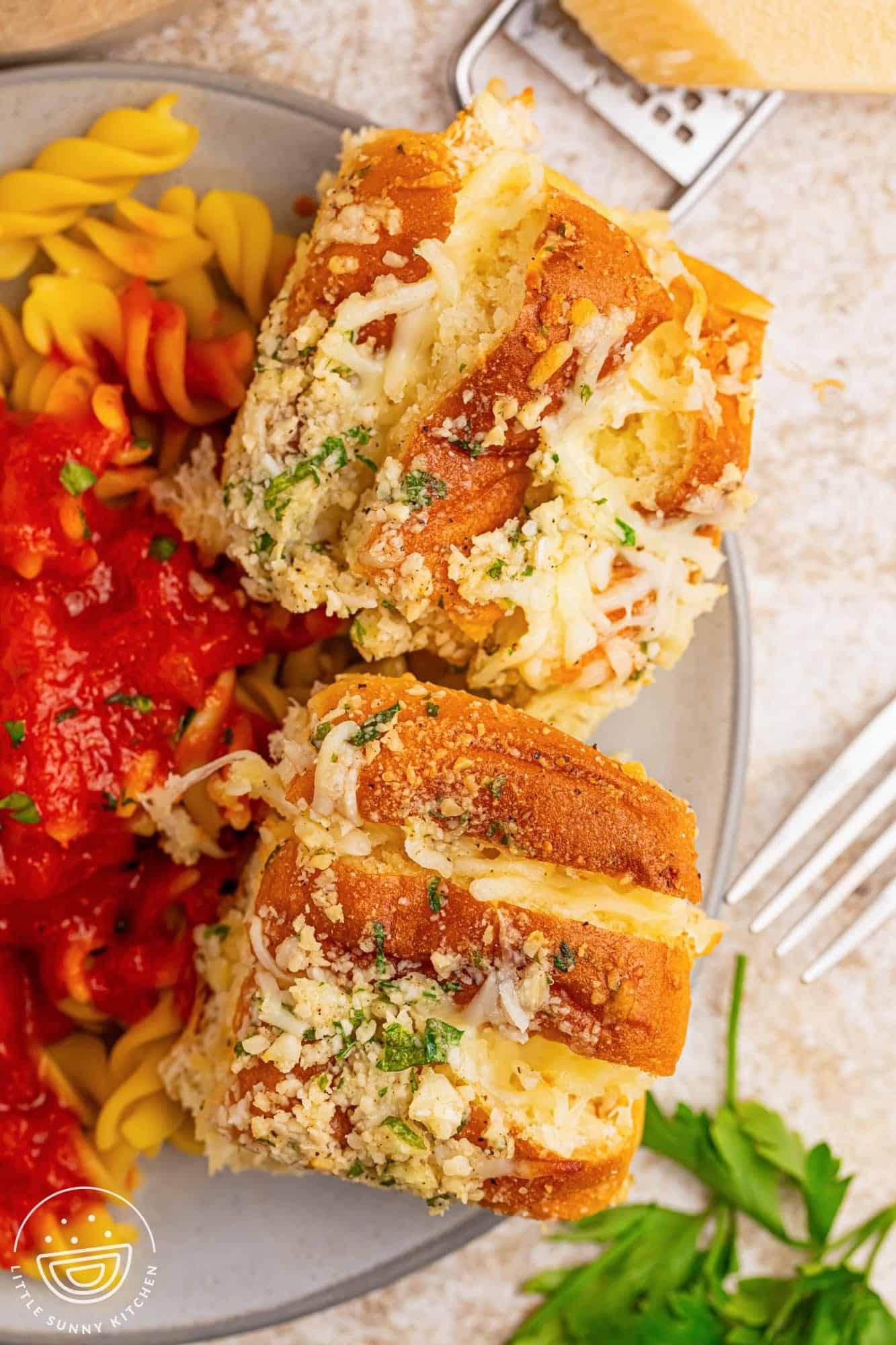 a plate of pasta with tomato sauce. On the side of the plate are two garlic bread hawaiian rolls.
