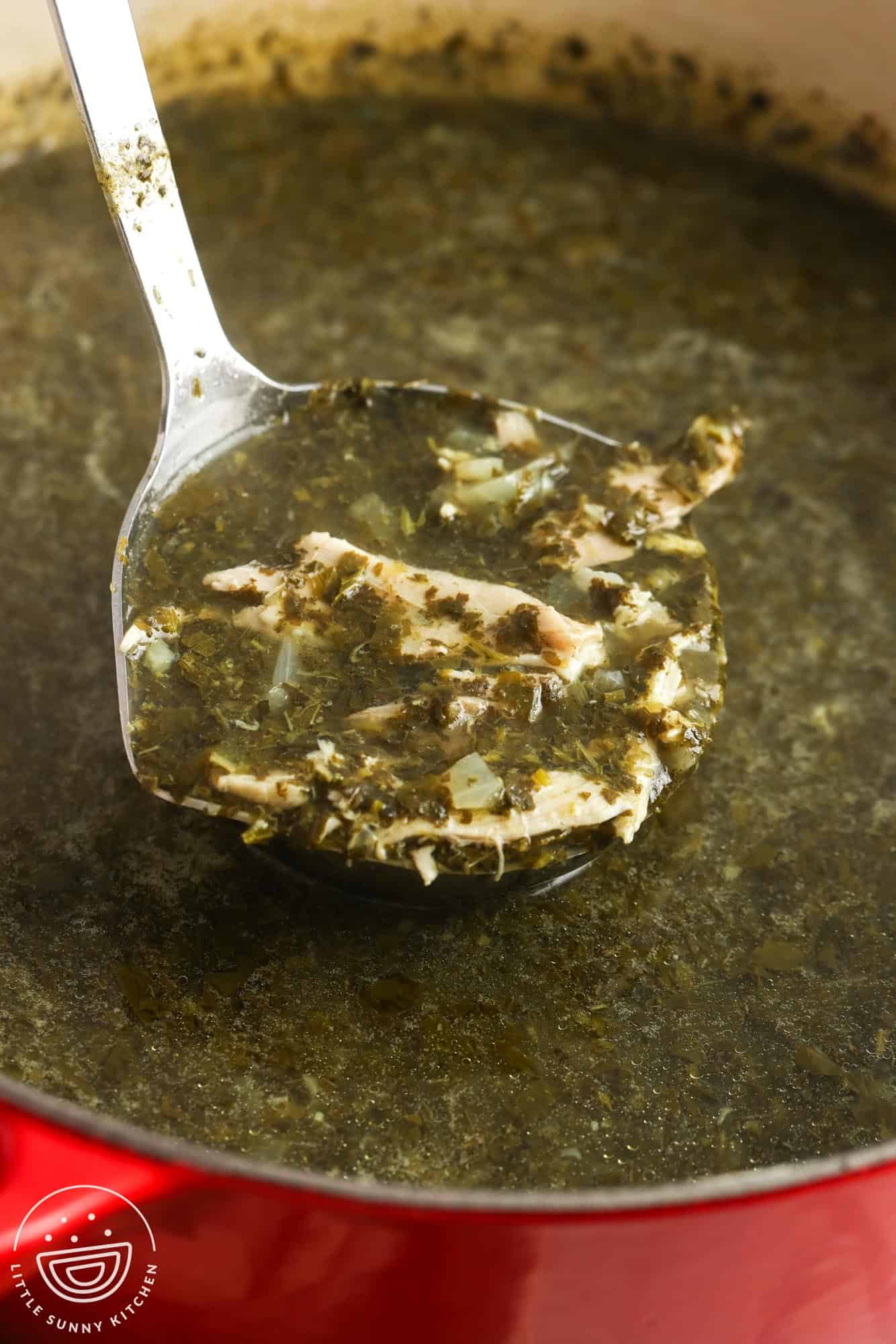 a ladle holding up a serving of molokhia with shredded chicken from a large pot.