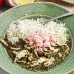 a green ceramic bowl of rice with molokhia, garnished with onions.