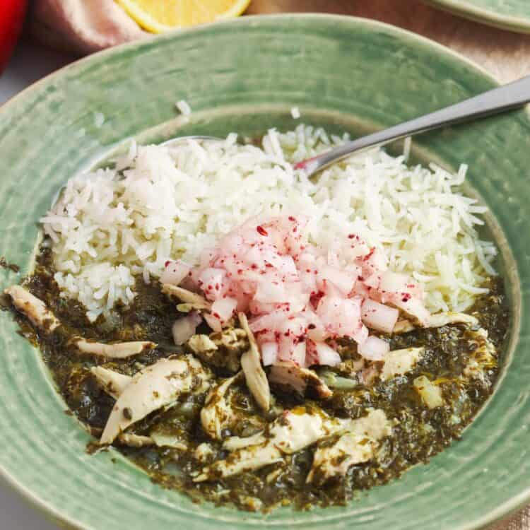 a green ceramic bowl of rice with molokhia, garnished with onions.