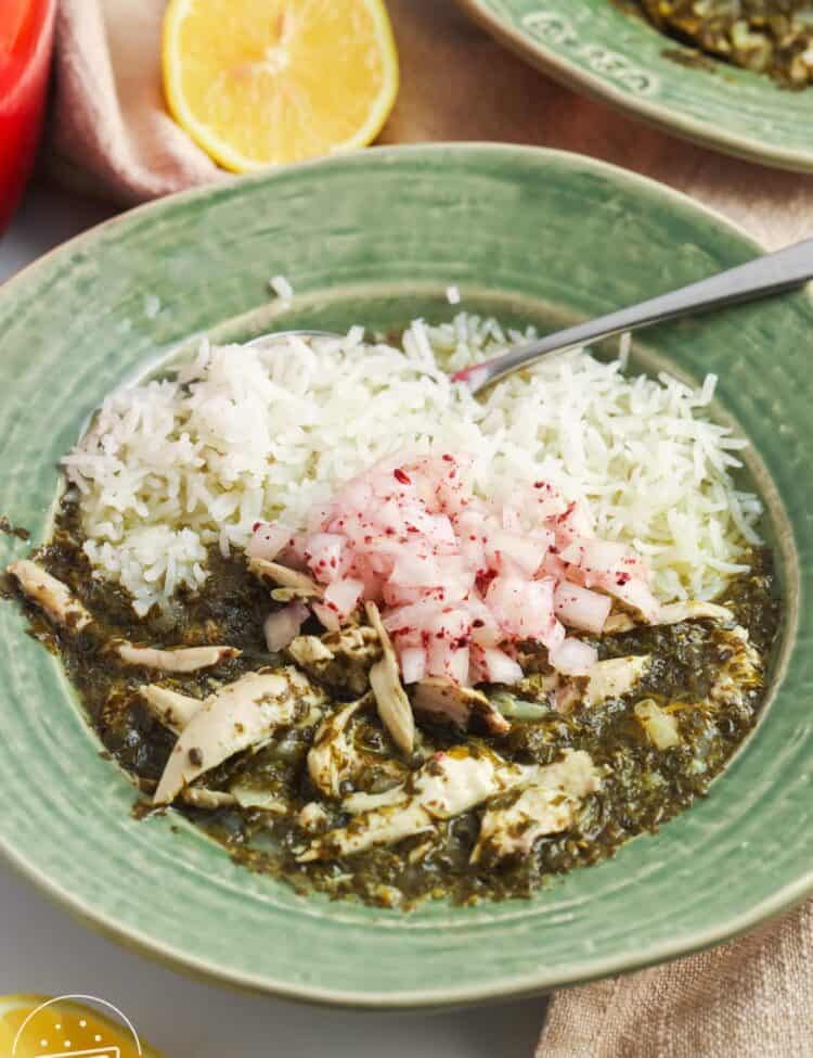 a green ceramic bowl of rice with molokhia, garnished with onions.
