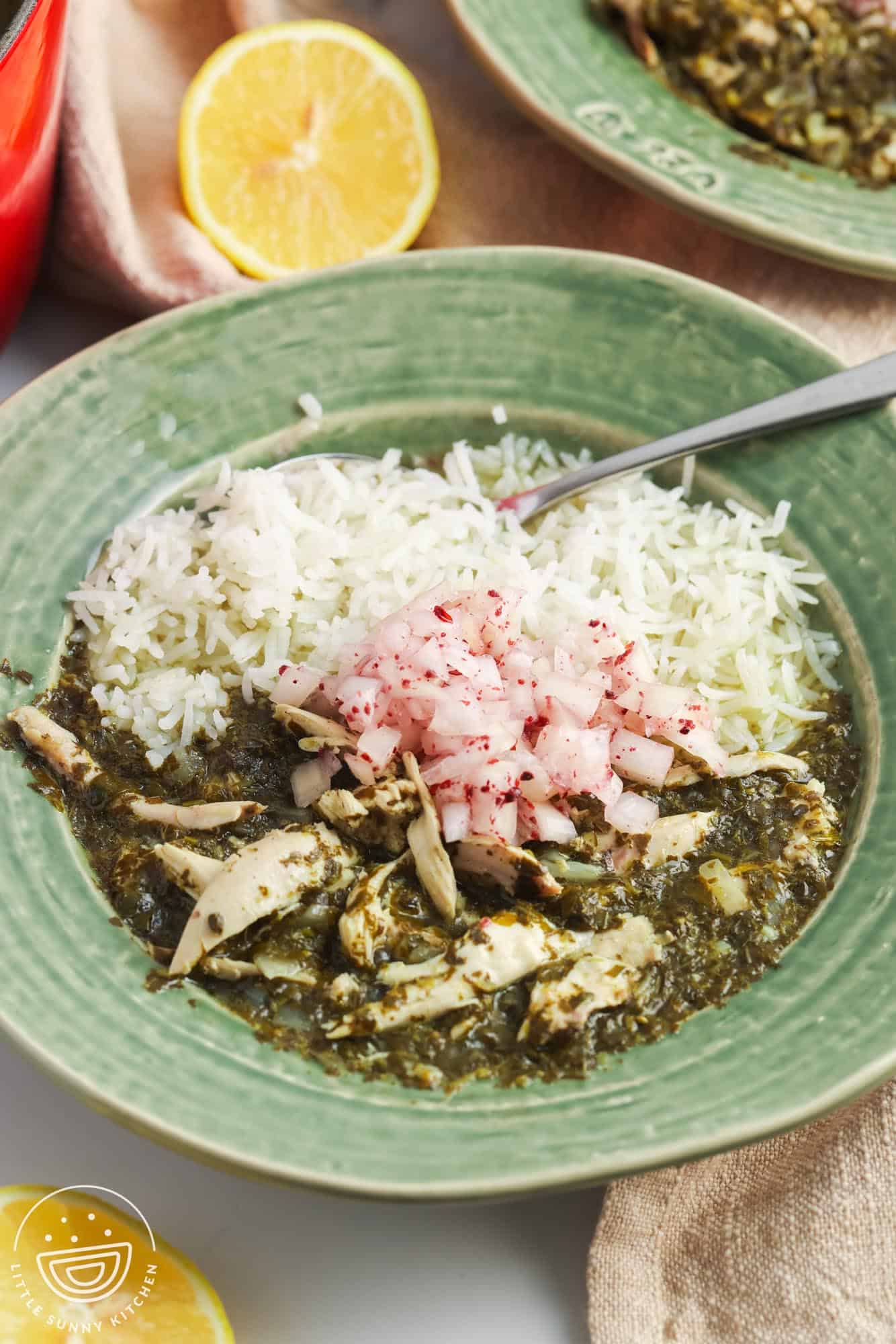 a green ceramic bowl of rice with molokhia, garnished with onions.