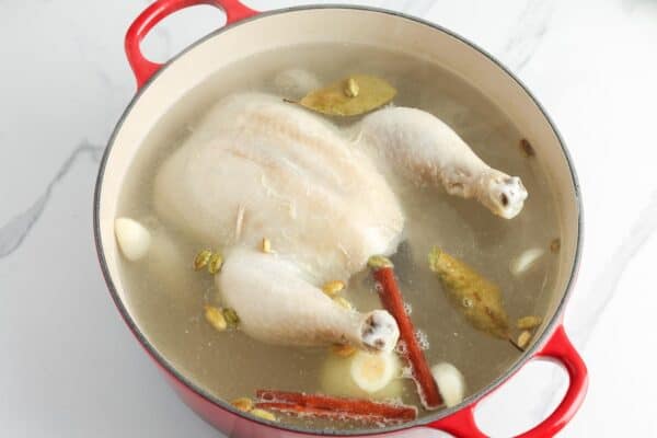 whole chicken poaching in a dutch oven with cinnamon and cardamom
