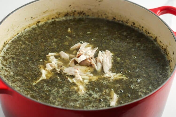 shredded chicken added to molokhia stew in a red dutch oven.