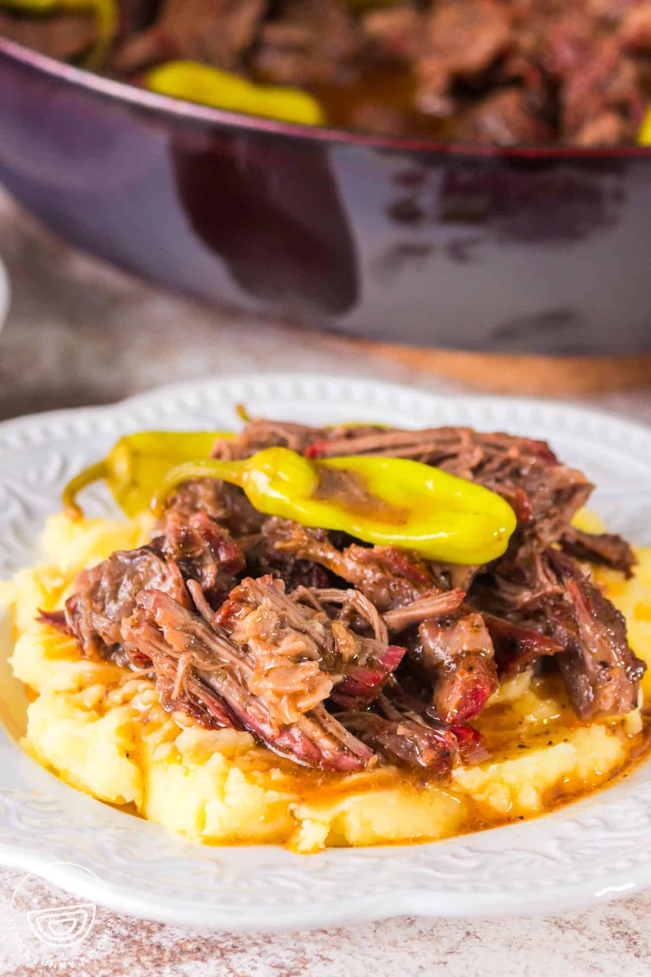 A white plate of mashed potatoes topped with smoked Mississippi pot roast.