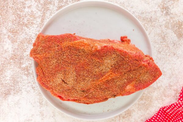 a raw chuck roast on a plate, rubbed with a spice blend.