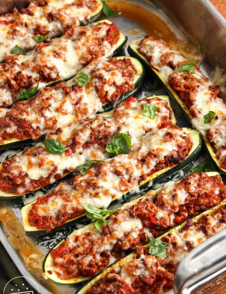 a roasting pan filled with zucchini ground beef zucchini boats topped with melted mozzarella cheese and fresh basil leaves.