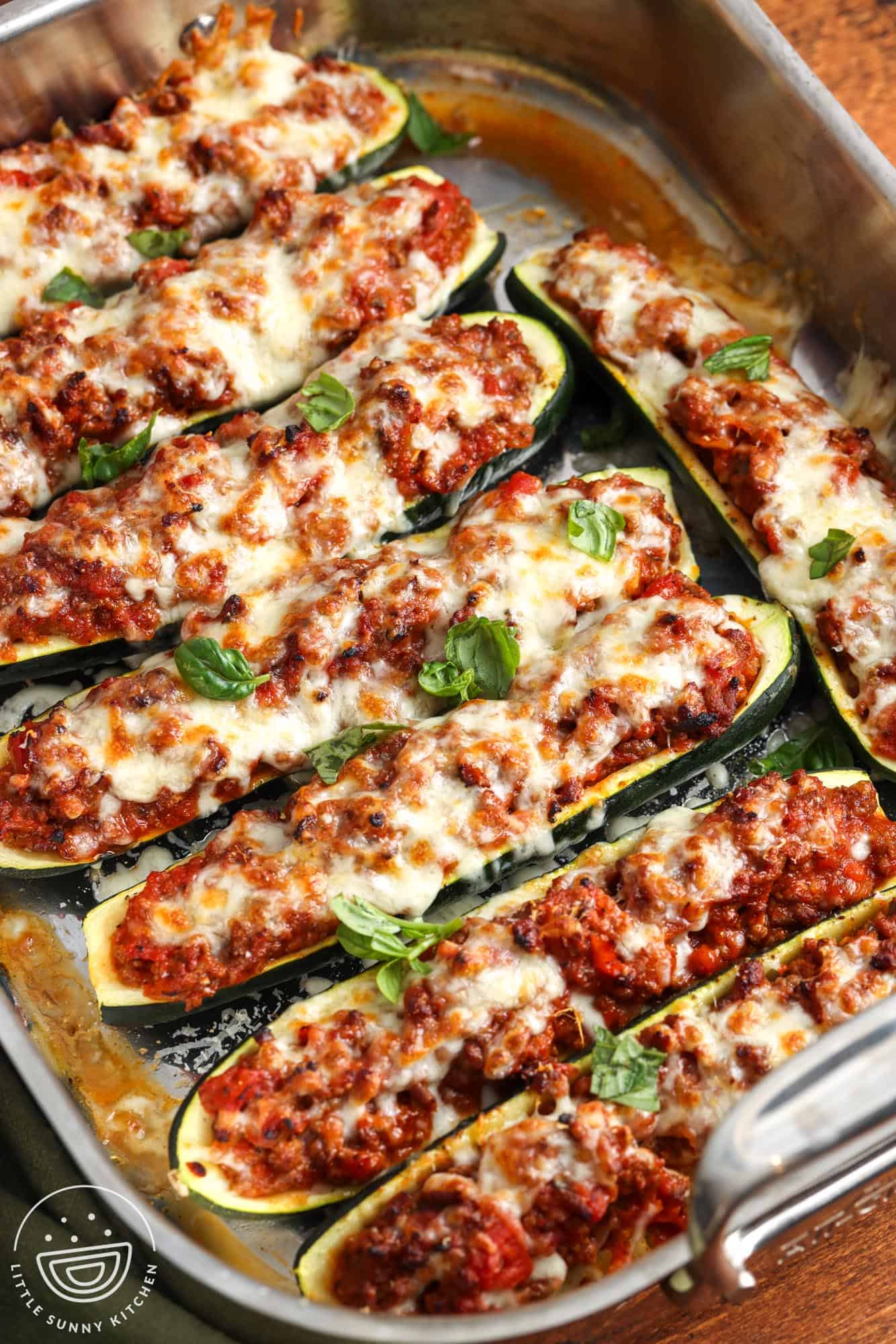 a roasting pan filled with zucchini ground beef zucchini boats topped with melted mozzarella cheese and fresh basil leaves.