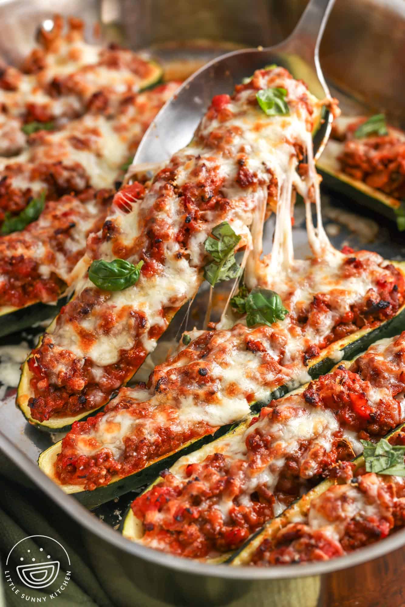 a large spoon lifting up a zucchini boat that is filled with beef and tomatoes and topped with melty cheese.