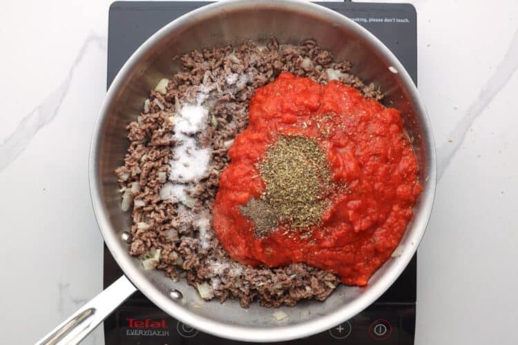 ground beef cooking in a skillet with onions seasonings and tomato sauce.