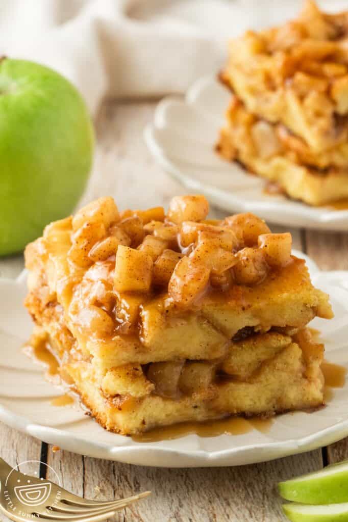 a square piece of apple bread pudding on a fluted white dessert plate. In the background is a green apple.