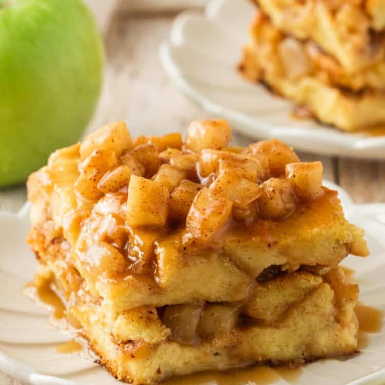 a square piece of apple bread pudding on a fluted white dessert plate. In the background is a green apple.