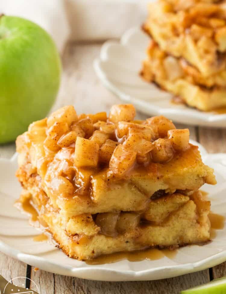 a square piece of apple bread pudding on a fluted white dessert plate. In the background is a green apple.