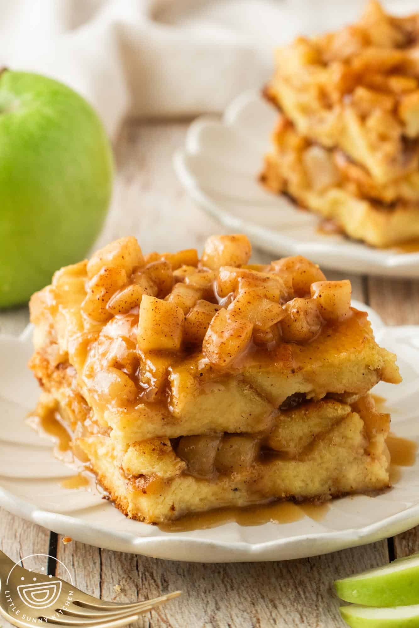 a square piece of apple bread pudding on a fluted white dessert plate. In the background is a green apple.