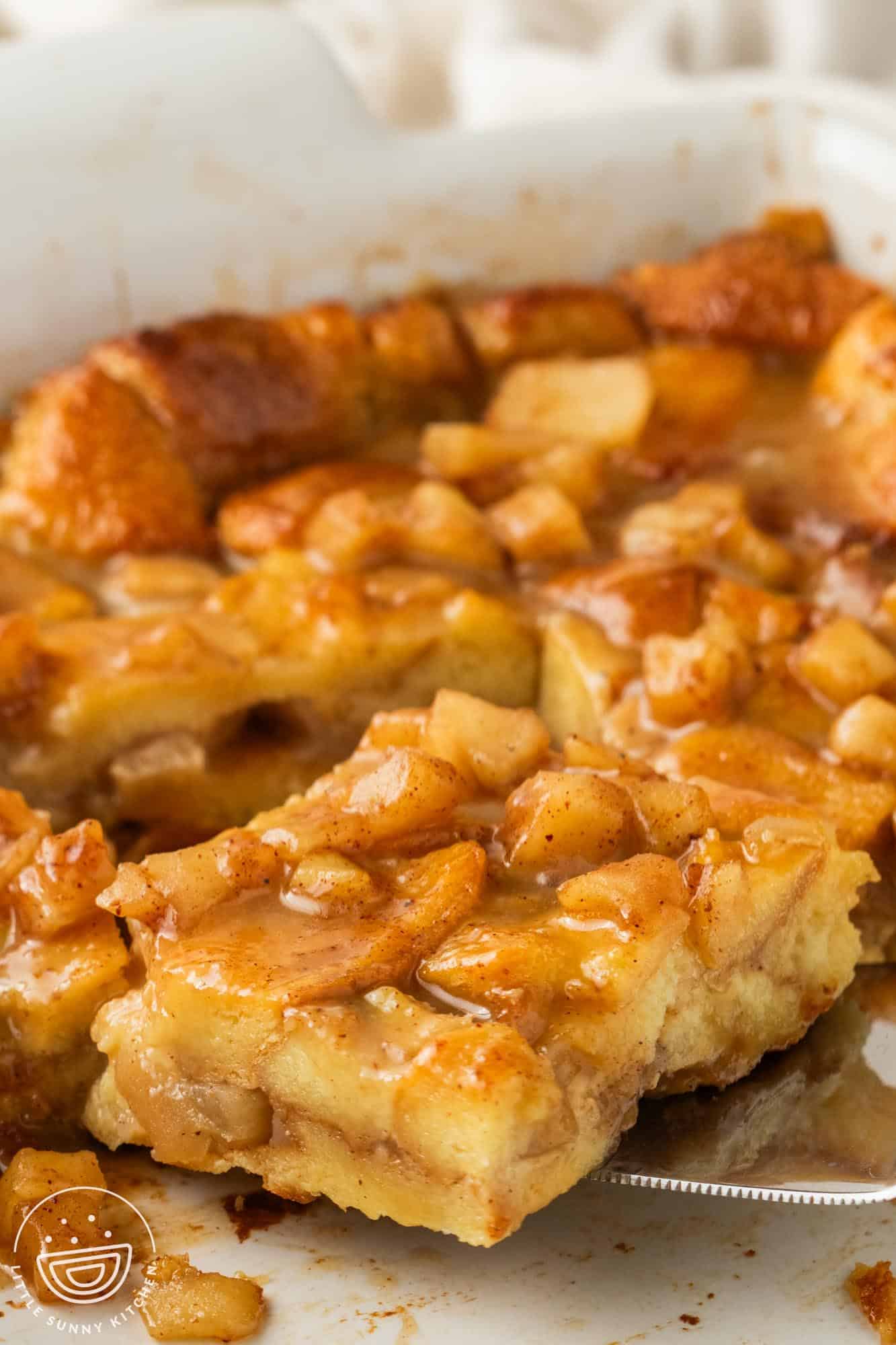 a slice of apple bread pudding with brown sugar glaze removed from the pan with a spatula.