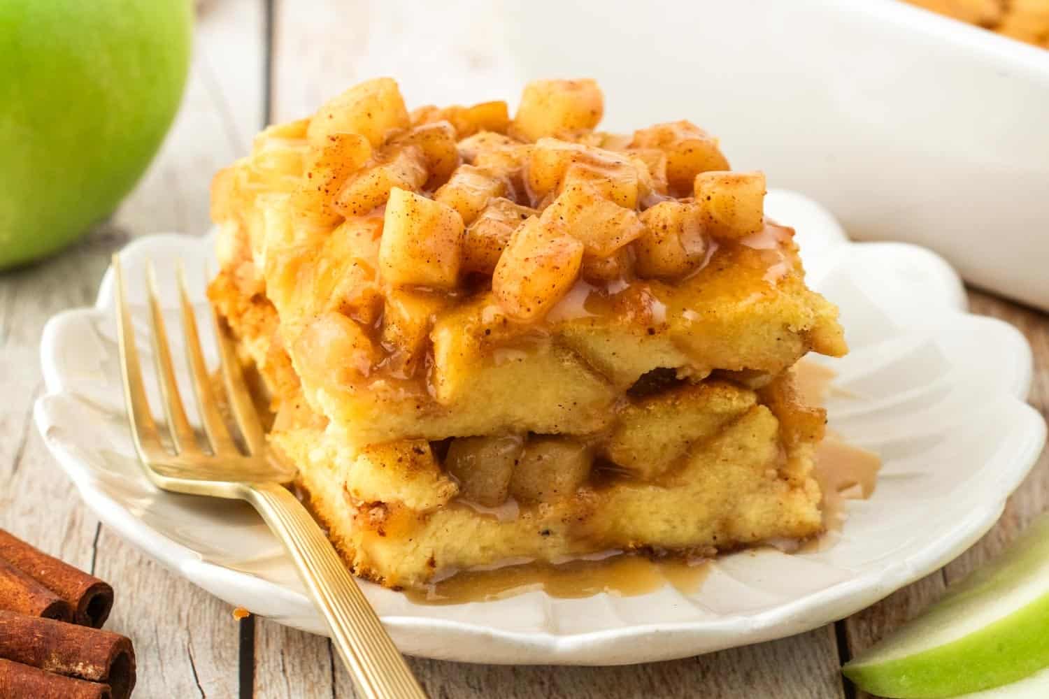 a square piece of apple bread pudding on a fluted white dessert plate. In the background is a green apple.