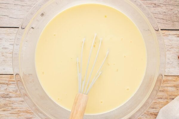 Custard base for bread pudding in a large glass bowl with a wire whisk.