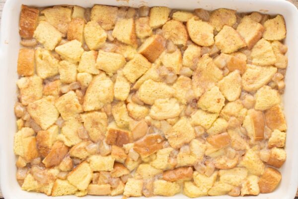 custard added to apple pie bread pudding mixture in a ceramic baking dish.
