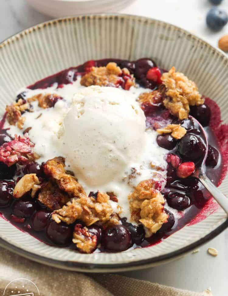 a bowl of blueberry crisp topped with a scoop of vanilla bean ice cream.