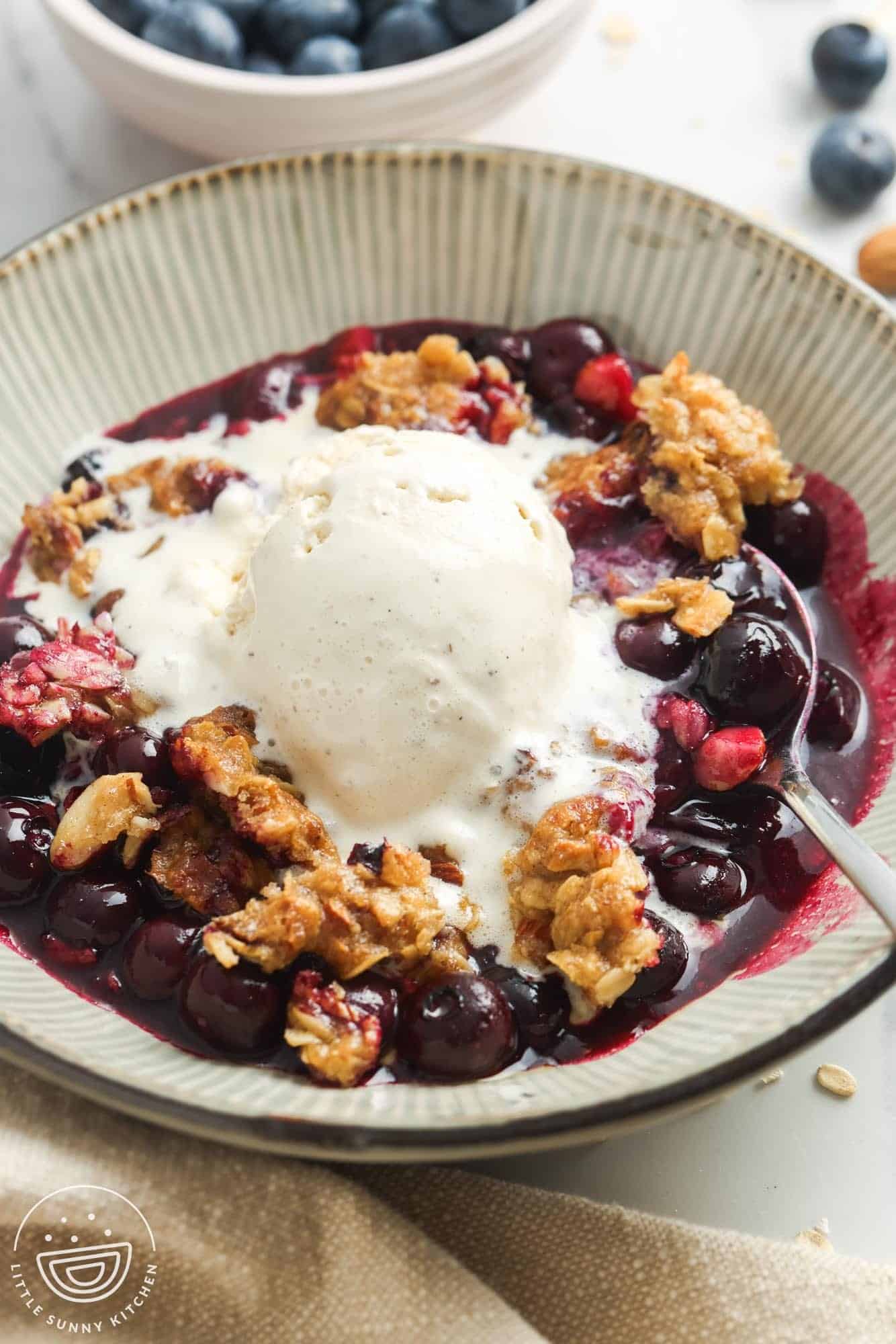 a bowl of blueberry crisp topped with a scoop of vanilla bean ice cream.