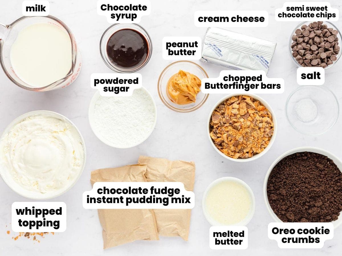 Overhead image showing labeled ingredients for no bake Butterfinger pie, including milk, chocolate syrup, cream cheese, semisweet chocolate chips, salt, chopped Butterfinger bars, peanut butter, powdered sugar, whipped topping, chocolate fudge instant pudding mix, melted butter, and Oreo cookie crumbs.