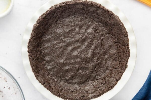 Pressed Oreo crust in a white pie dish, ready for chilling.