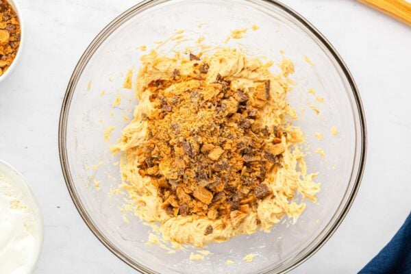 Chopped Butterfinger candy added on top of the peanut butter mixture in a mixing bowl.