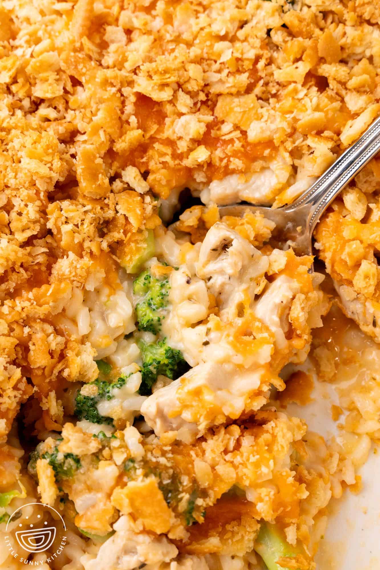 closeup of a creamy chicken broccoli rice casserole. a spoon is lifting up a serving.