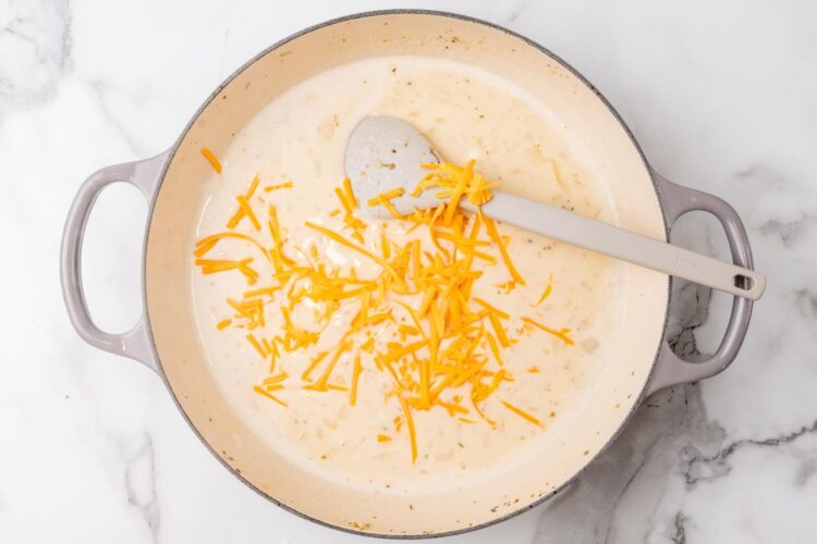 a creamy sauce with shredded cheddar, cooking in a skillet.