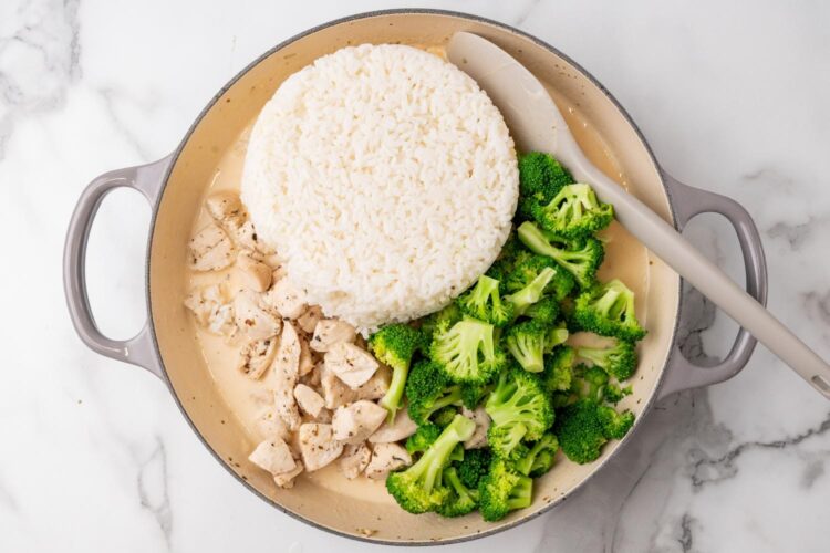 cooked white rice, cooked chicken, and broccoli added to a creamy sauce in an enameled cast iron pan.