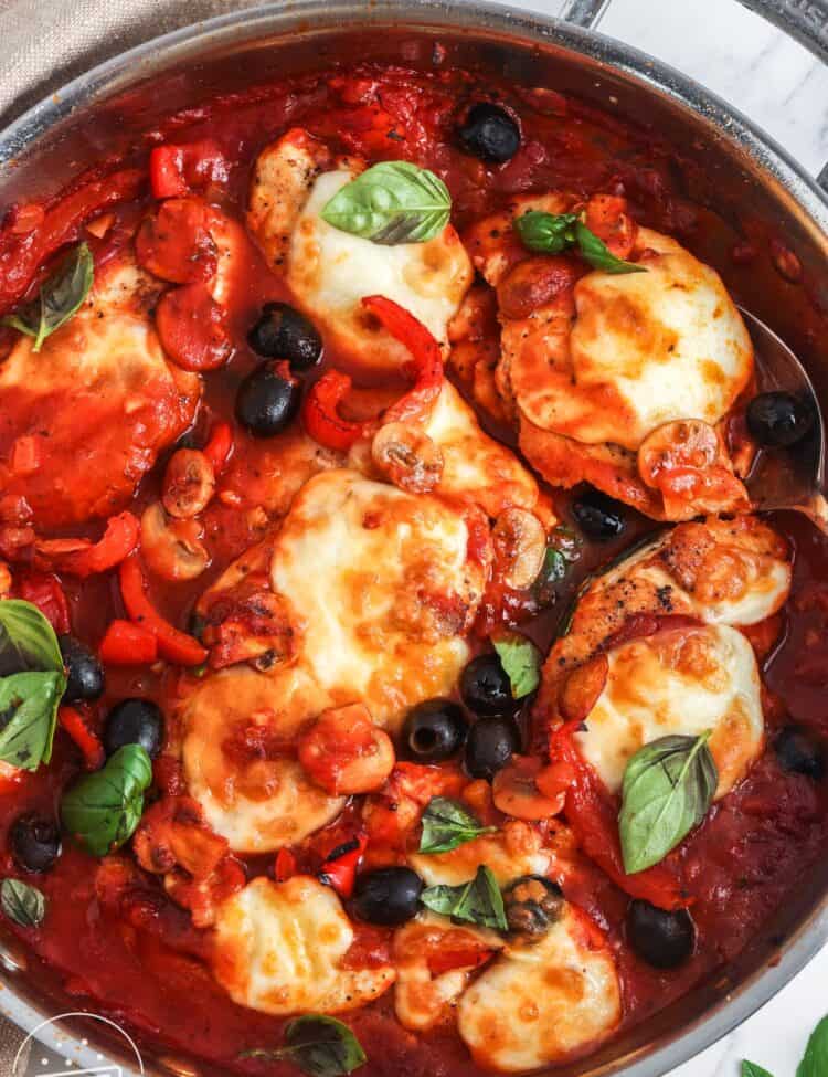 a stainless steel skillet of chicken pizzaiola with olives, mushrooms, and cheese.