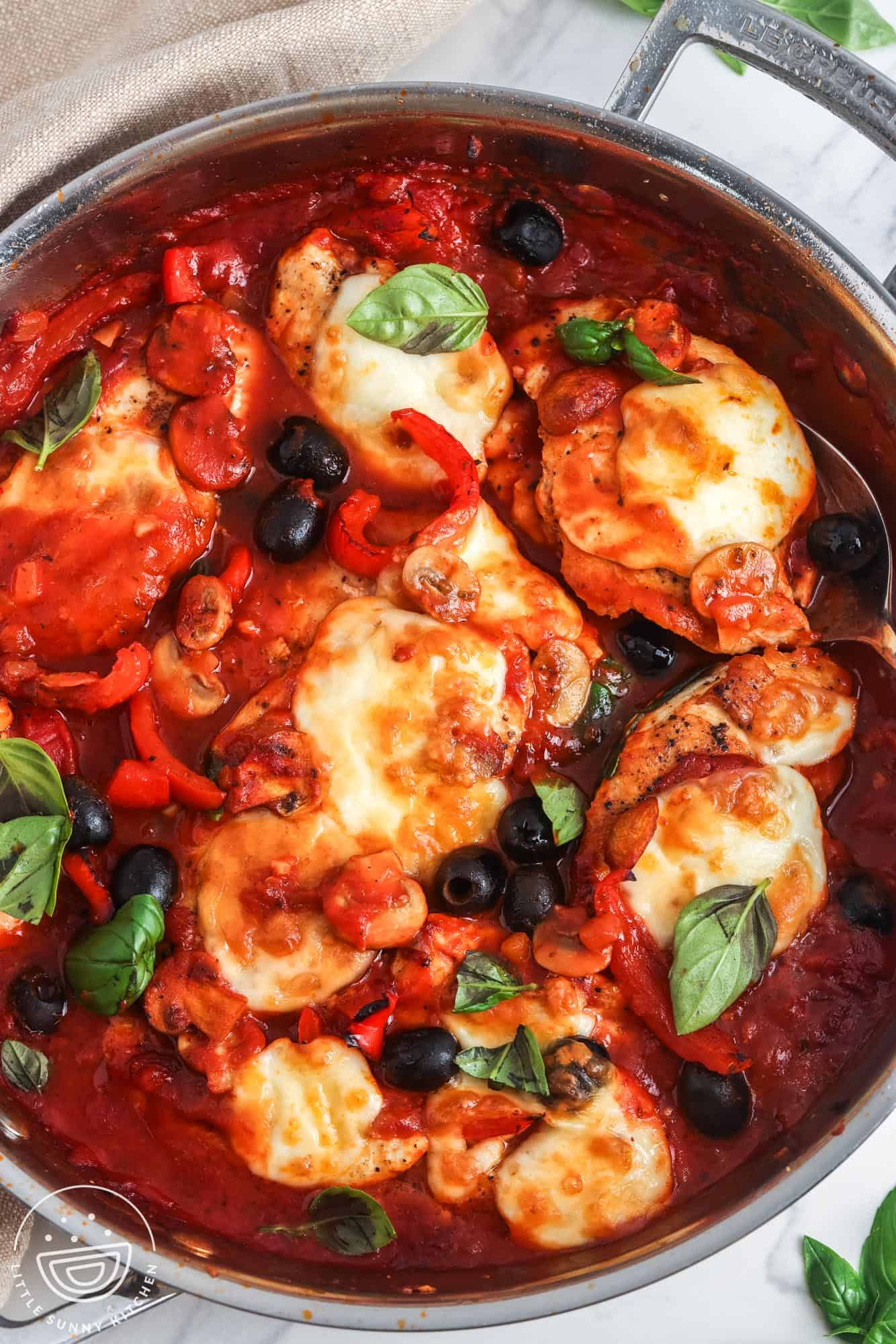 a stainless steel skillet of chicken pizzaiola with olives, mushrooms, and cheese.