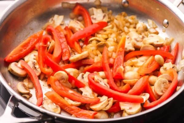 onion, sliced red pepper, and sliced mushrooms sauteing in a skillet.