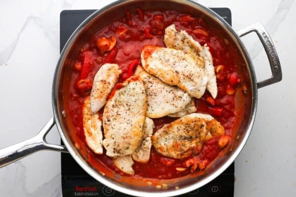 seared chicken cutlets added to veggies and tomato sauce in a skillet.