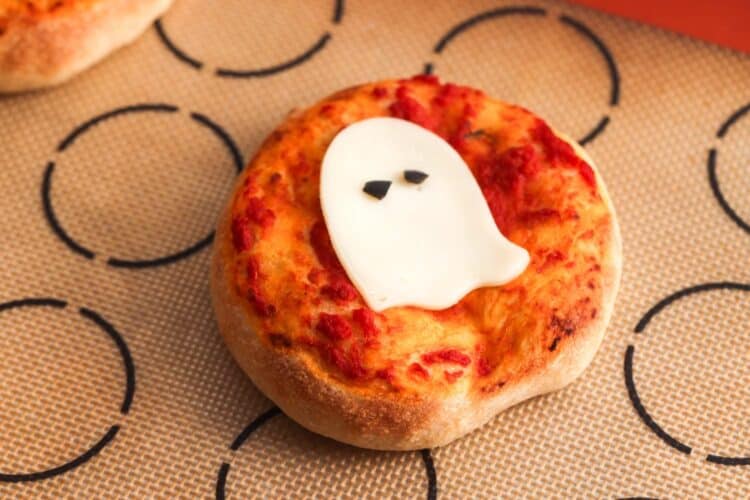 Baked mini pizza topped with a mozzarella ghost shape and olive eyes placed after baking.