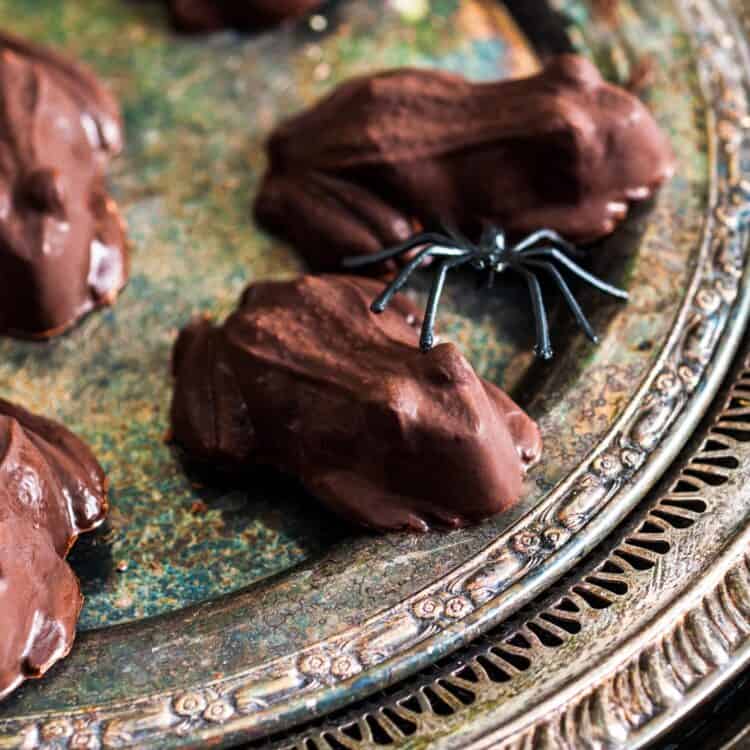 Close-up of homemade chocolate frog candies on an antique silver tray, with a small plastic spider decoration for a spooky Halloween touch.