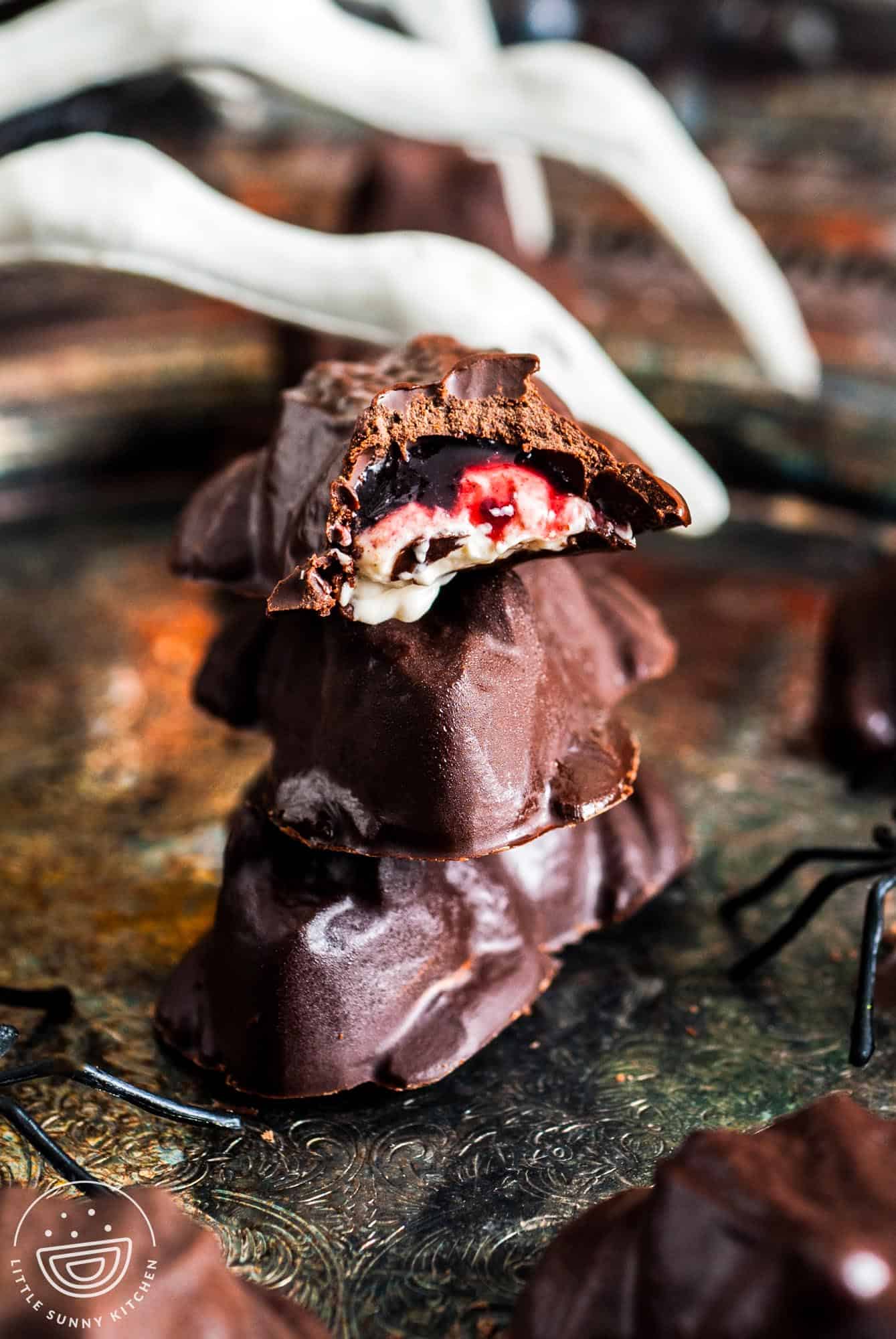 Stacked chocolate frog candies with the top one cut open to reveal a gooey cheesecake and blackberry jam filling, displayed on a vintage tray with Halloween decor.