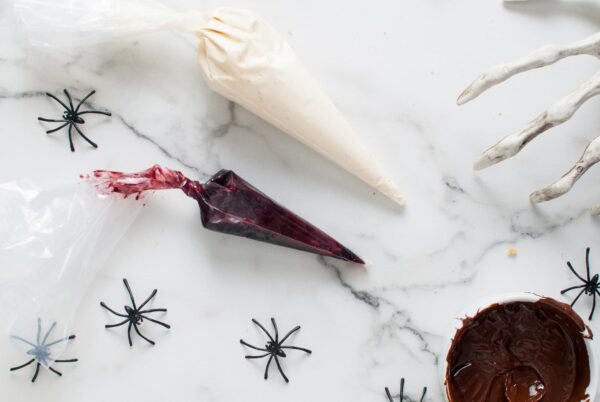 Two piping bags on a marble surface—one with cheesecake filling and one with blackberry jam surrounded by plastic spiders.