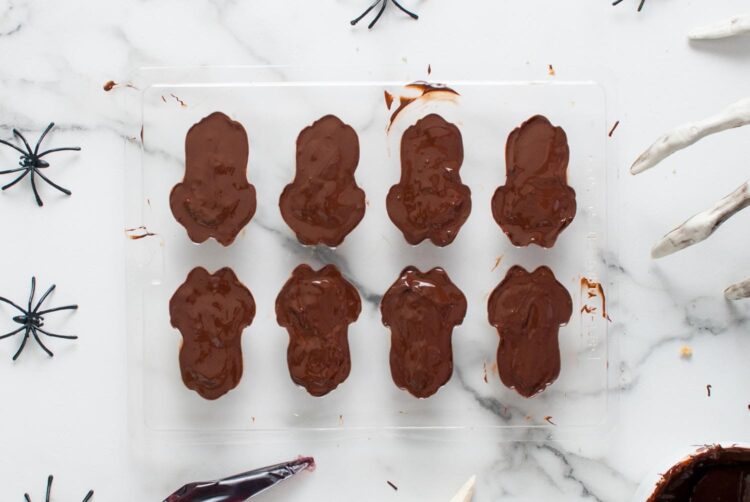 Filled frog-shaped chocolate molds sealed with a final layer of melted chocolate, ready to be chilled and set for the final candy shape.
