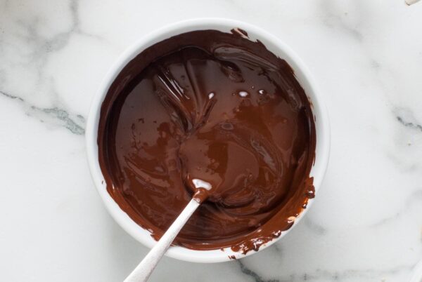 A bowl of melted chocolate with a spoon, smooth and glossy, ready for molding.