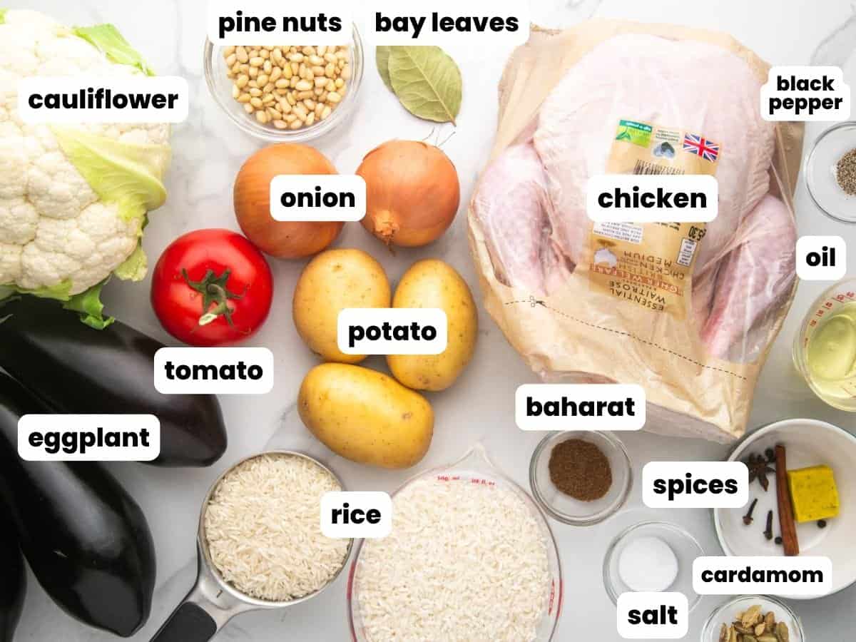 Ingredients for maqluba, arranged on a marble counter. Included is a whole chicken, vegetables, pine nuts, two types of rice, and spices.