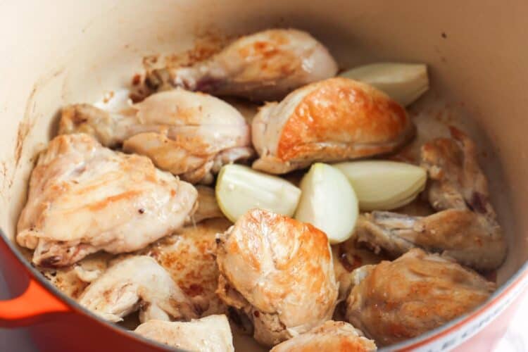 seared chicken pieces in a dutch oven with quartered onions.