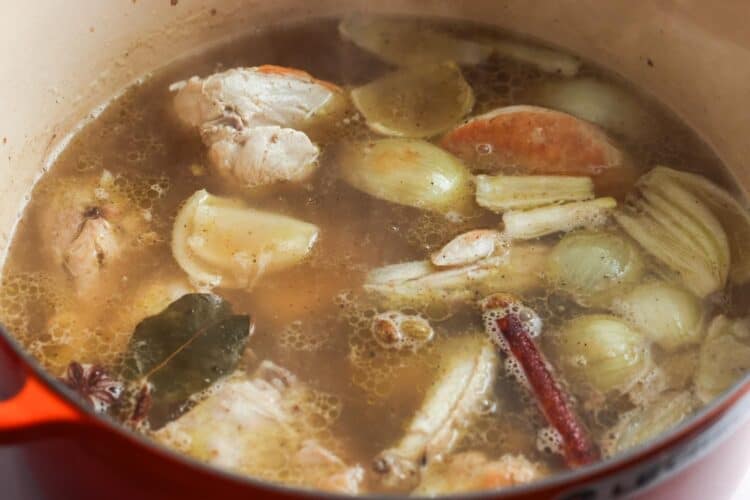 chicken simmering in spiced broth in a dutch oven for maqluba.