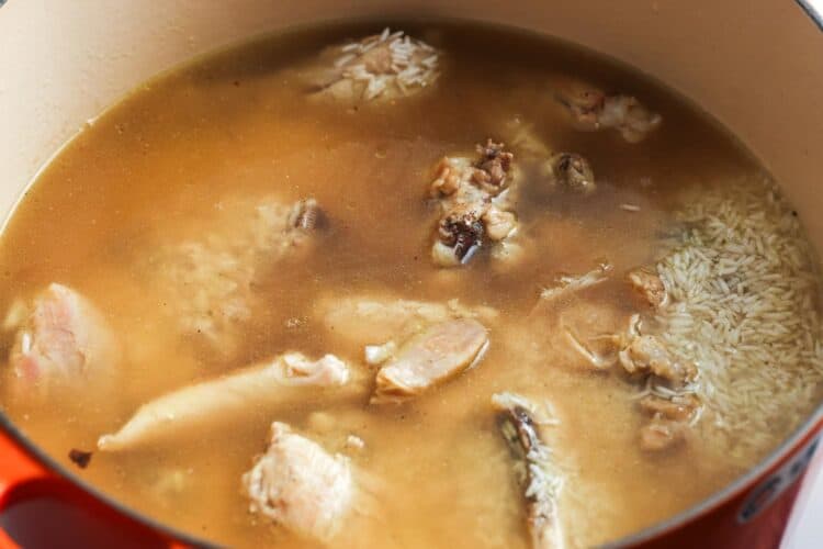 Rice and broth added to a dutch oven with veggies and chicken for maqluba.